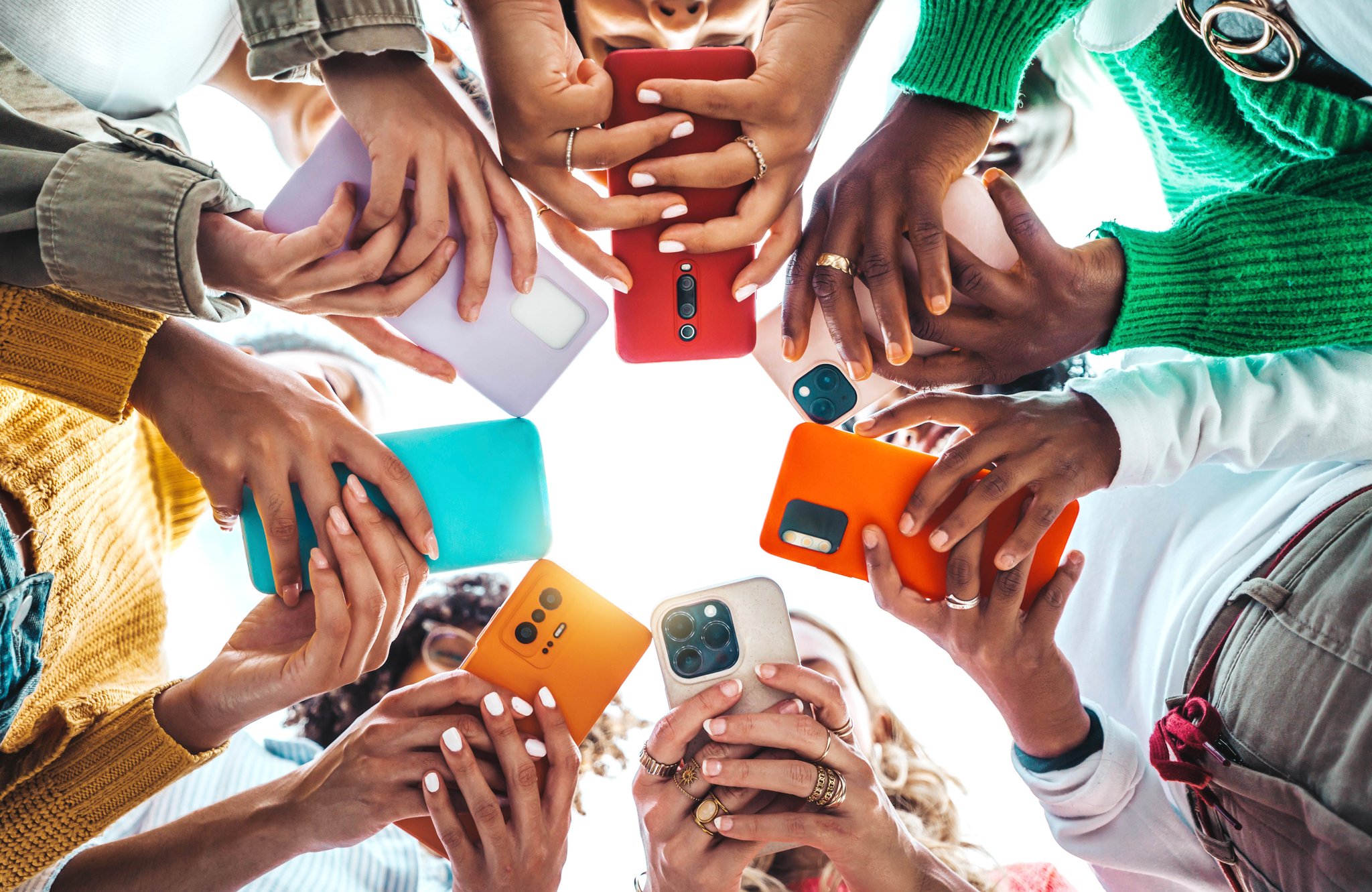 Diverse group of people holding colorful smartphones in a circle, reflecting mobile engagement enabled by customer rewards API documentation