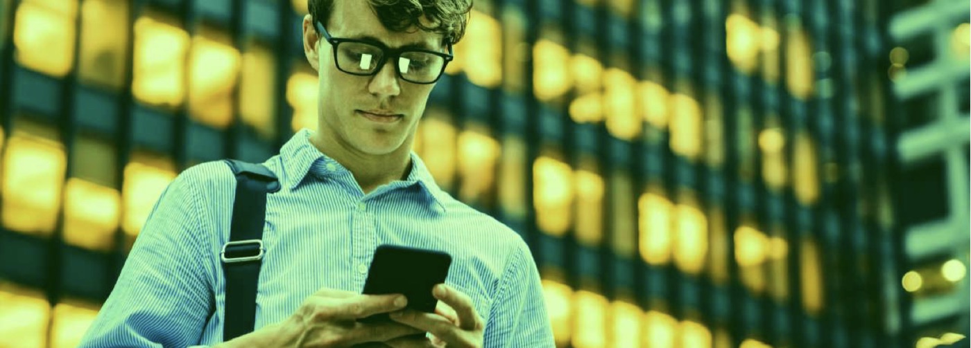 A person looking at a smartphone in front of a lit building
