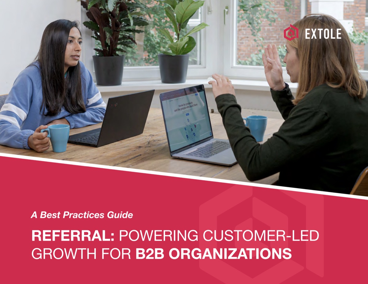 Two colleagues talking across a table with laptops on the cover of Extole's referral best practices guide for B2B organizations