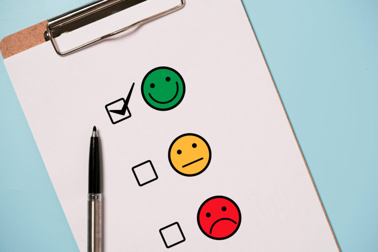 Clipboard page with three colored smiley faces (green happy, yellow neutral, red unhappy) and several checkboxes. A pencil rests beside the sheet.