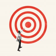 Businessman reaching toward a red bullseye target on a light background, symbolizing aiming for a goal.