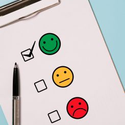 Clipboard page with three colored smiley faces (green happy, yellow neutral, red unhappy) and several checkboxes. A pencil rests beside the sheet.